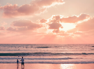 A pink sunset in pastel colors at the sea with a family playing ball