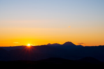 淡いグラデーションの黄昏の空と遠くの山の稜線に光る太陽。