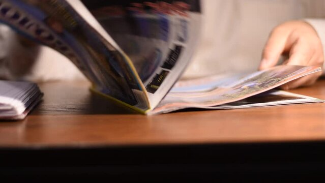 A man sits at a table and flips through the pages of a magazine.