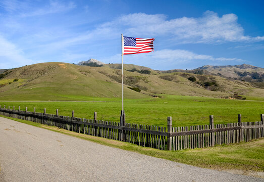 Patriotic scene of American flag flying above a fence on a ranch
