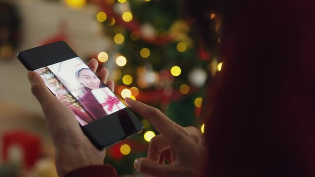 Close-up Asia female blogger hold phone screen select photo post on social media made online greeting christmas new year card on platform enjoy celebration in house full of decoration light indoors.