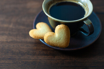 Two heart-shaped biscuits and a coffee cup with a saucer on a rustic wooden floor, selective focus, empty space for text. Valentine's day concept.