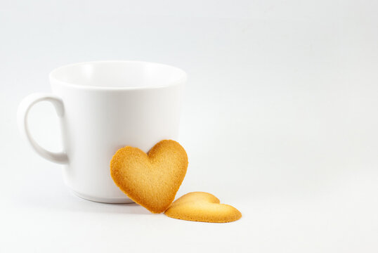 Two heart-shaped biscuits and a mug of coffee on a white background, empty space for text. Valentine's day concept.