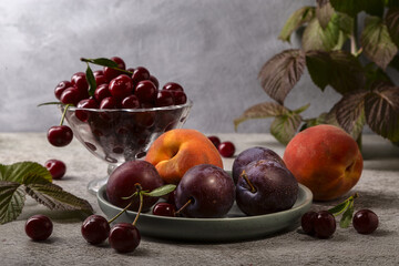 Cherry in a vase, peach and plum on a plate on a gray table