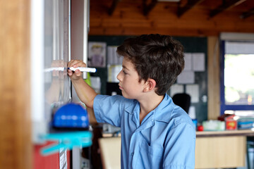Young school boy writing on a white board in classroom