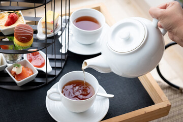 Woman hand pouring afternoon tea from the teapot to a cup. Traditional drink in the garden with snacks.