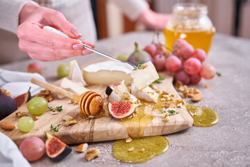 Woman puts on a fork piece of Camembert or brie cheese at domestic kitchen