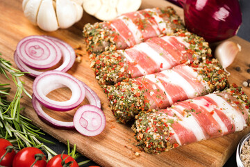 Balkan cevapcici or Romanian mititei. Traditional Balkan food. Raw minced meat rolls wrapped with bacon with seasonings and vegetables around on wooden cutting board