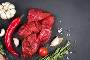 Chopped raw beef or lamb meat with seasonings, chili pepper and vegetables over dark concrete background with copy space. Veal meat for cooking stew, azu or other meat main dish