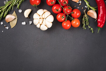 Variety of seasonings, herbs and vegetables over dark concrete background - food background with copy space for text. Garlic, tomatoes, chili pepper and rosemary