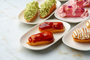 Set of colored eclairs with whipped cream on white plates