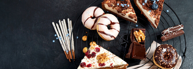 Table with various cookies, donuts, cakes, cheesecakes on dark background.