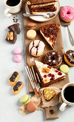 Table with various cakes, cookies, donuts and coffe cups on light background.