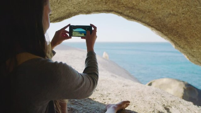 Beach, cave and woman with phone for picture, photography and memories of holiday, vacation and scenic view. Travel, smartphone and girl enjoying freedom, journey and adventure on rock by ocean