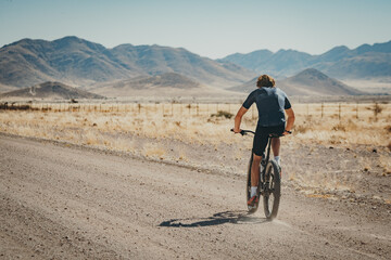 Panorama - Ein einzelner Fahrradfahrer fährt mit seinem MTP entlang einer einsamen Straße im Naukluft Gebirge, Namibia