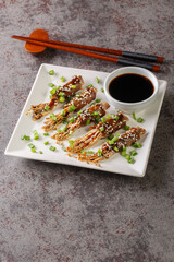 Japanese beef and enoki mushrooms rolls with teriyaki sauce close-up in a plate on the table. Vertical