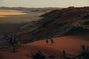 Fototapeta na wymiar Zwei Mädchen laufen bei Sonnenuntergang durch den roten Sand der Elim Düne - Im Hintergrund die Weite des Sossusvlei, Sesriem, Namibia