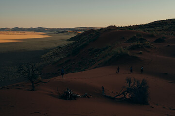 Fototapeta na wymiar Frau und ihre drei Kinder laufen bei Sonnenuntergang durch den roten Sand der Elim Düne - Im Hintergrund die Weite des Sossusvlei, Sesriem, Namibia