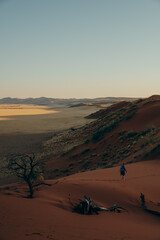 Fototapeta na wymiar Frau läuft bei Sonnenuntergang durch den roten Sand der Elim Düne - Im Hintergrund die Weite des Sossusvlei, Sesriem, Namibia