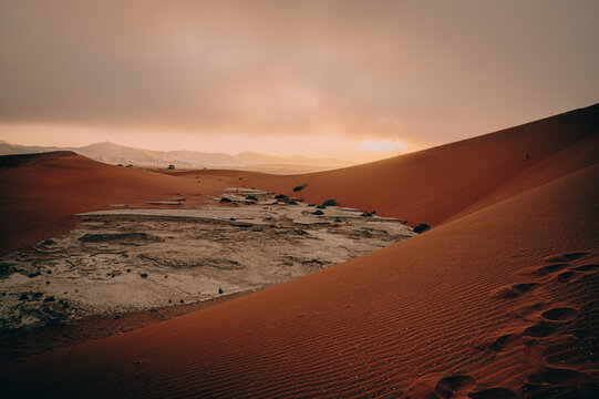 Blick von der D&uuml;ne Big Daddy in ein Vlei mit seinem wei&szlig;en rissigen Ton-Schluff - die aufgehende Sonne durchflutete den Morgennebel und sorgt f&uuml;r eine magische Lichtstimmung, Sossusvlei, Namibia