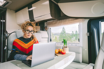Independent woman sitting inside a camper van in smart remote working job activity using laptop. Concept digital nomad freedom lifestyle with female people writing on computer. Outdoors view outside
