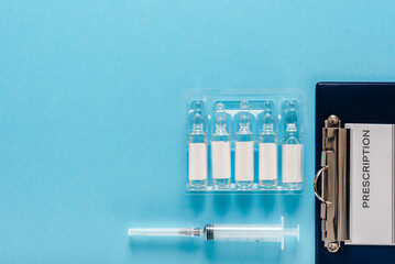 Vials with medication, syringe and medical prescription on blue flat background