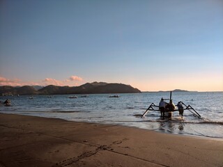 Fishermen pushing a traditional wooden fishing boat into the sea