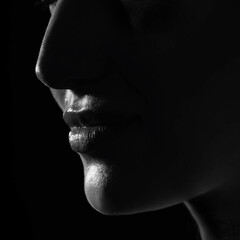 Fashion, beauty and make-up concept. Close-up dark face silhouette of beautiful and sexy woman. Part of model face covered in shadow. Sensual mood. Lips in camera focus. Black and white image