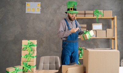 male warehouse worker seller in leprechaun hat, small stock business owner holding smartphone,...