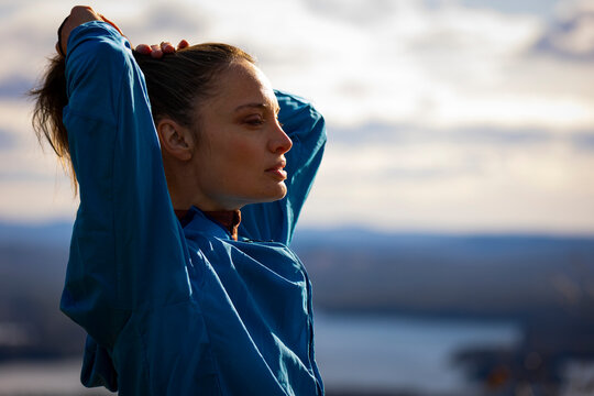 A woman in a blue jacket fixes her hair overlooking a Lake