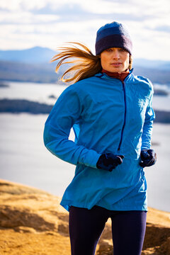 A woman  runs in the mountains with a lake in the back
