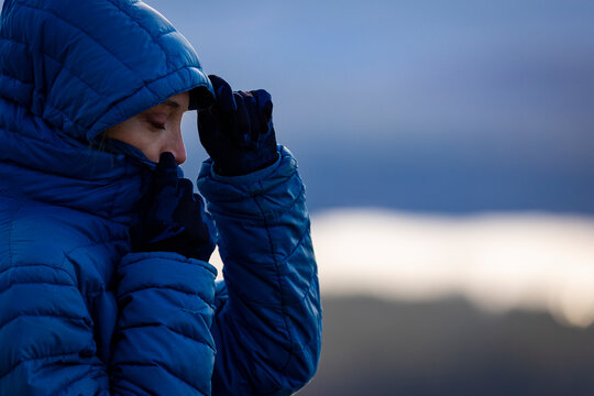 A woman in a blue down jacket huddles for warmth