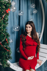 A young pregnant mother is sitting on a swing in a Christmas atmosphere