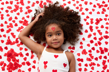 Little girl with afro hair lying on bed with heart shaped confetti on forehead
