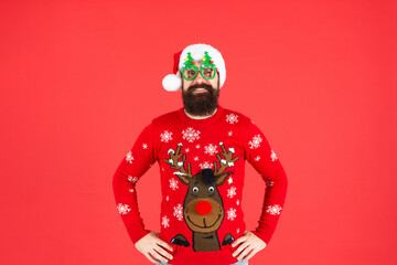 positive brutal hipster man in santa hat with party glasses on red background, xmas