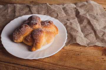 Pan de muerto on a white plate isolated on a wooden table. Typical mexican dessert.