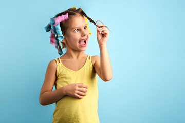 Little girl with curlers on blue background with copy space