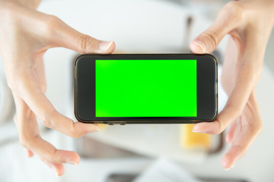 closeup hand holding smartphone top view in restaurant with blank space green screen colored