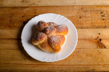 Pan de muerto on a white plate isolated on a wooden table. Typical mexican dessert.