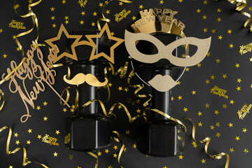 Two heavy dumbbells dressed up for New Year's Eve celebration party. Healthy fitness flat lay composition with golden decorations. Gym, workout Happy New Year resolution concept.