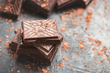 Dark chocolate bar pieces on dark background with grated chocolate and spices, pile chunks of broken chocolate