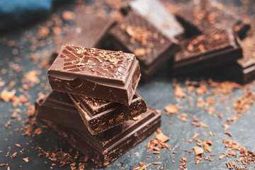 Dark chocolate bar pieces on dark background with grated chocolate and spices, pile chunks of broken chocolate
