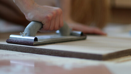 Carpenter grinders sanding wooden board. Close up of hands