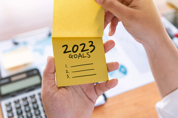 Hand of businesswoman holding yellow note paper 2023 goals message, Change and business goals for...