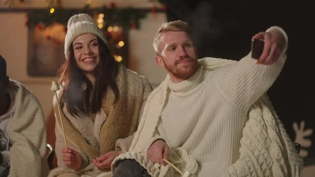 bearded man and pretty woman take video selfies in Christmas party in backyard, warm near fire