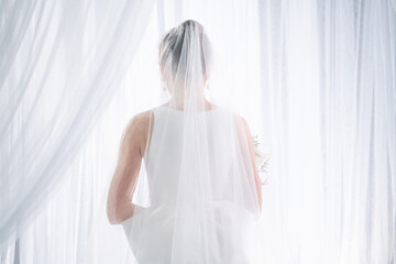 bride in white dress Standing by the window with white curtains
