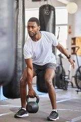 Fotobehang Sportschool Exercise, kettlebell and black man doing fitness with a weight with strength, focus and motivation. Sports, exercising and strong African male athlete doing muscle training or workout at a gym  © Lune V A/peopleimages.com