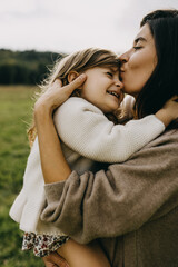 Closeup portrait of mother and daughter. Mother hugging little girl, holding in arms, kissing forehead.