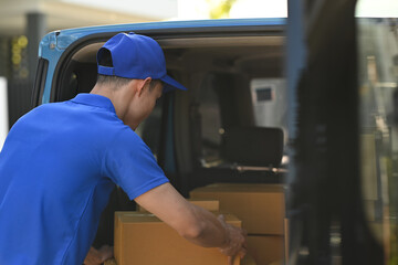 Back view of delivery men unloading cardboard boxes from cargo van. Delivery service, delivery home and shipping concept