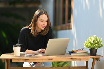 Beautiful caucasian woman having remote work on laptop computer while sitting at outdoors
